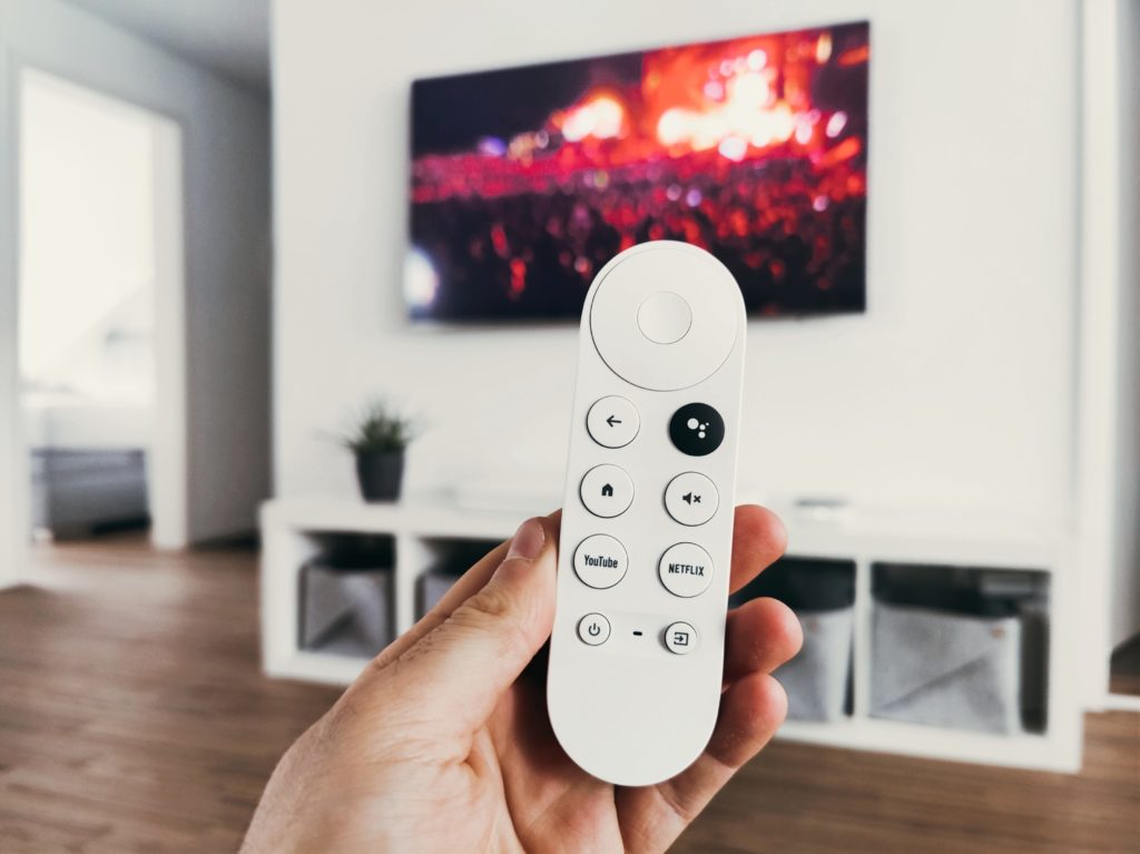 Hand holding connected TV remote in front of TV screen